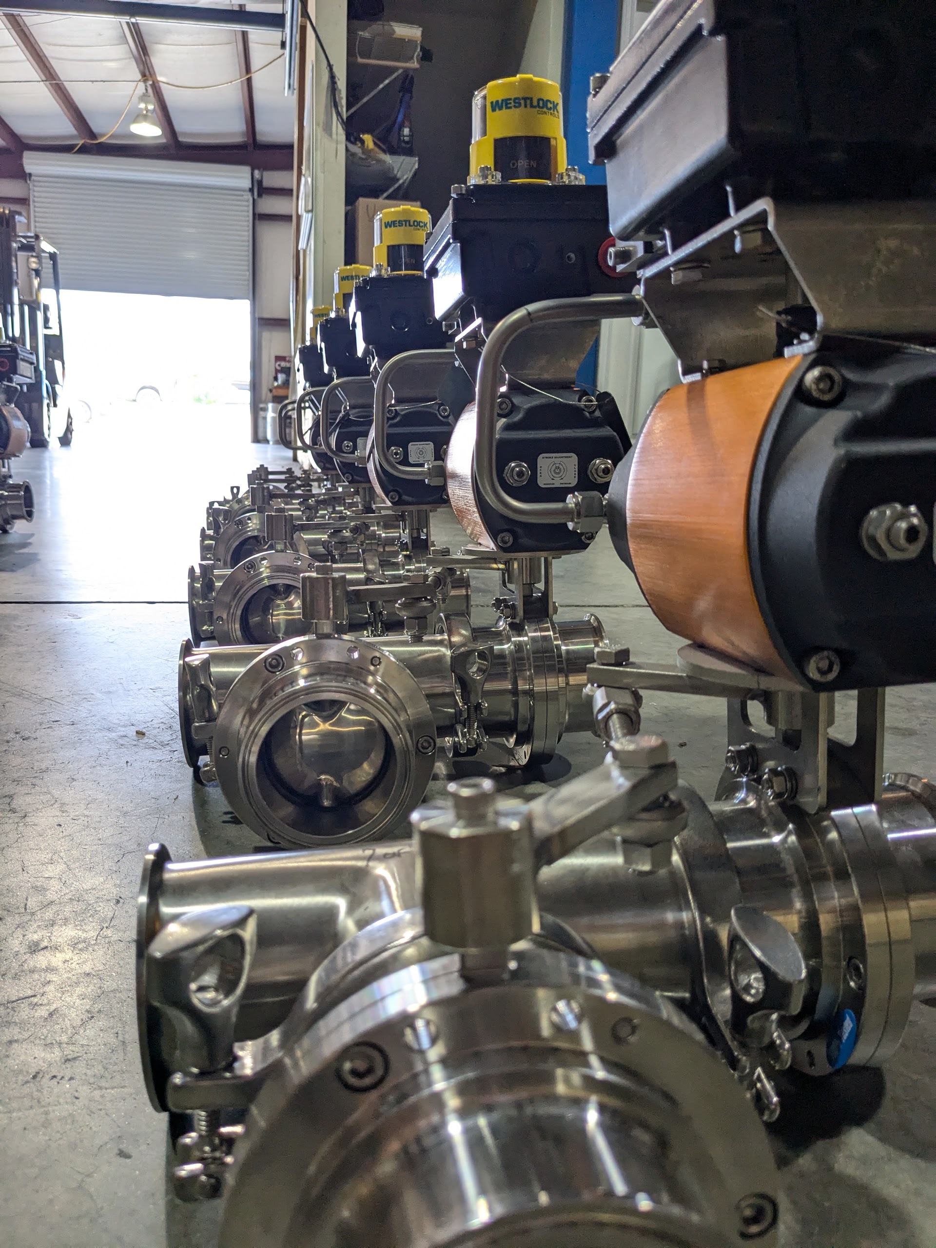 Row of stainless sanitary valve assemblies with position monitors staged on the shop floor